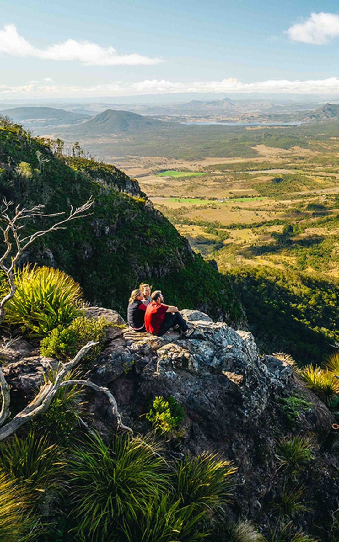 Two people seated on a Scenic Rim escarpment overlooking the mountain landscape.