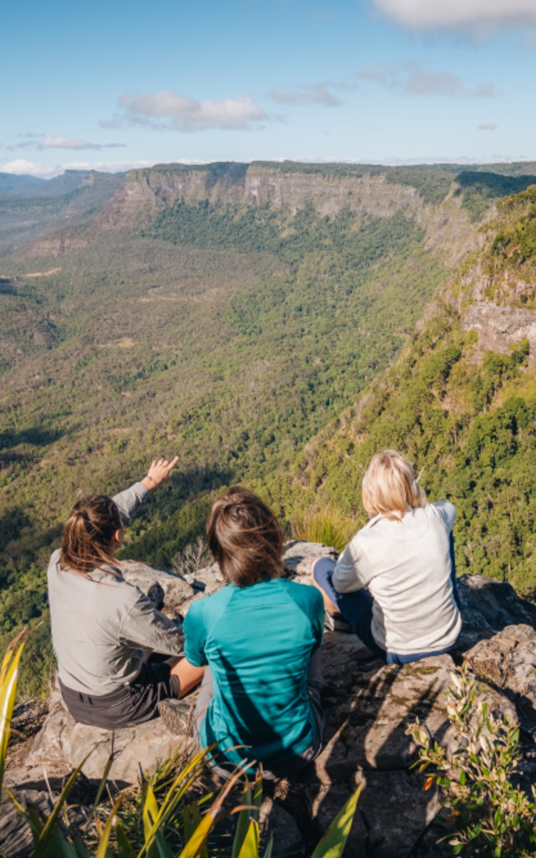 Three people seated at a Scenic Rim lookout above a forested escarpment.