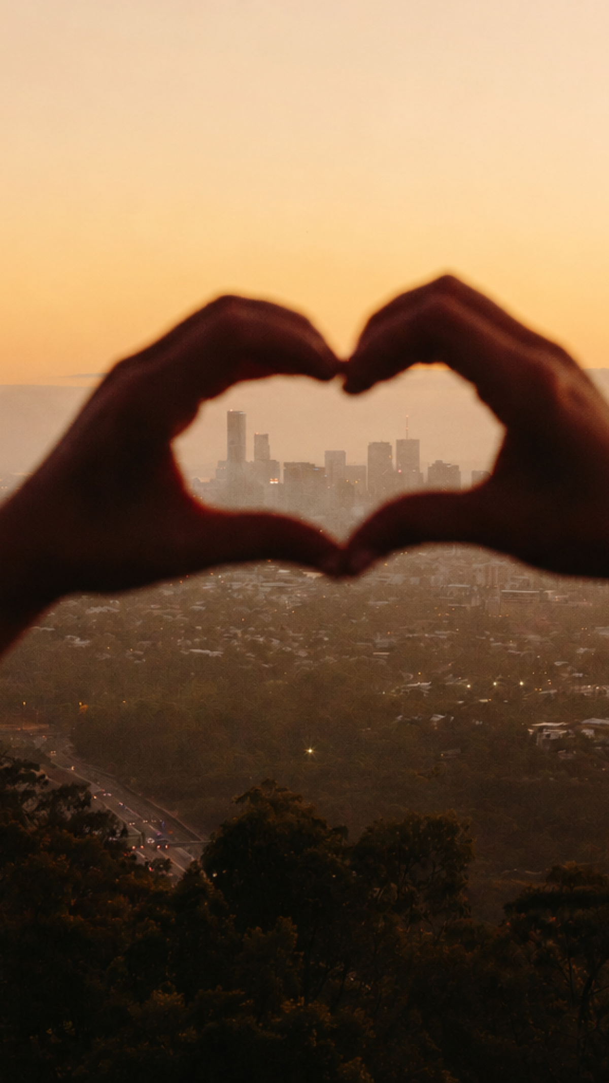 Person framing a heart around Brisbane at sunset