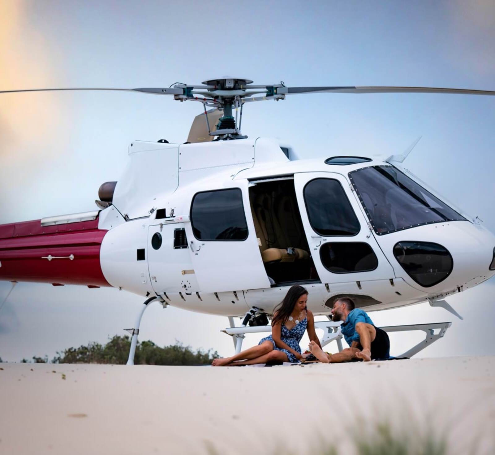 Couple seated beside a Bekaa Air helicopter on the beach.