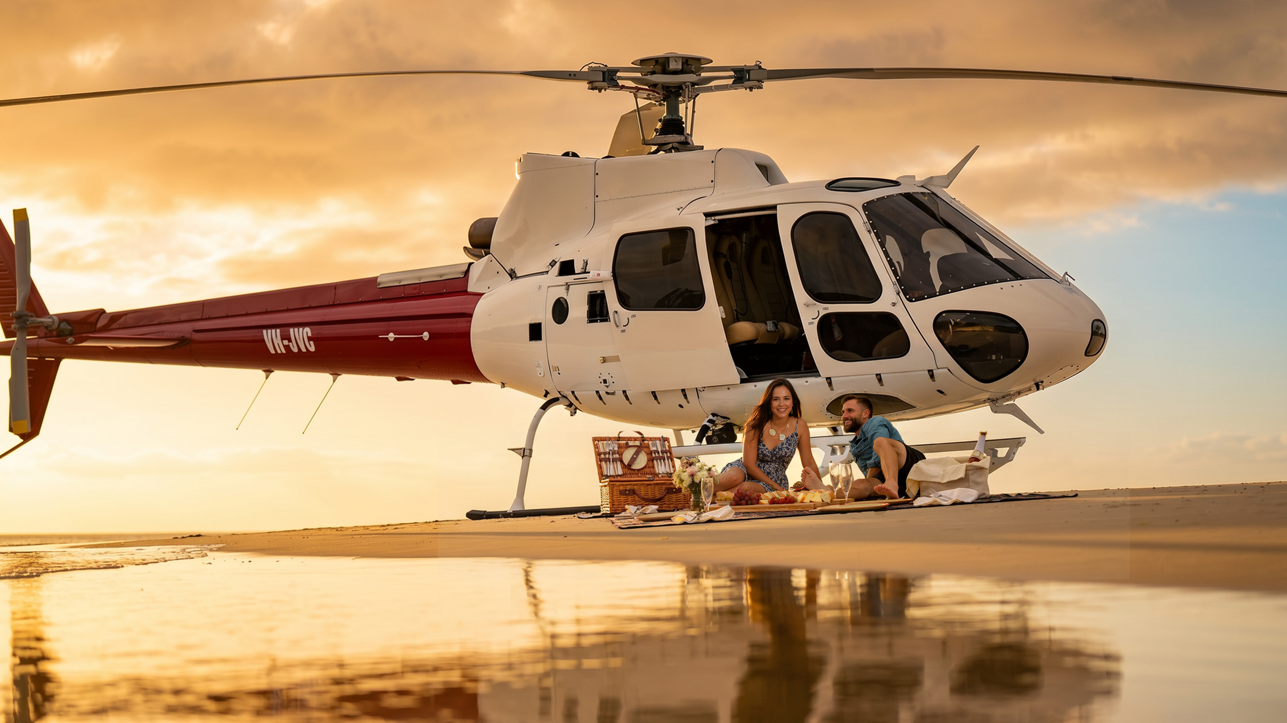 Couple enjoying a beach picnic beside a Bekaa Air helicopter at sunset.