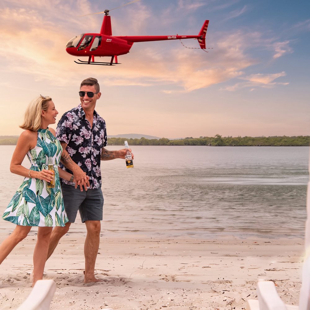 Couple enjoying drinks on an island beach with a Bekaa Air helicopter overhead