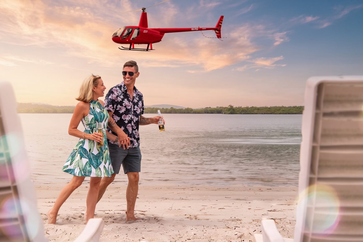 Couple enjoying drinks on an island beach with a Bekaa Air helicopter overhead