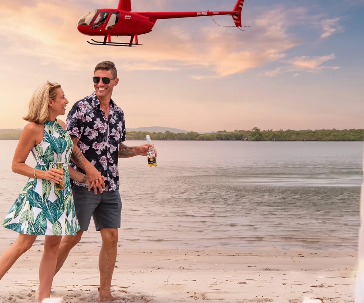 Couple enjoying drinks on an island beach with a Bekaa Air helicopter overhead
